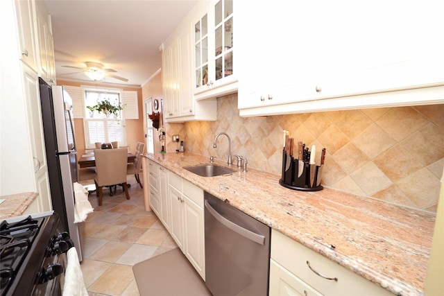 kitchen featuring light stone counters, a sink, appliances with stainless steel finishes, backsplash, and glass insert cabinets