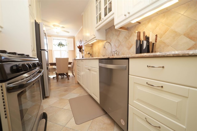 kitchen with light tile patterned floors, stainless steel appliances, light stone countertops, tasteful backsplash, and glass insert cabinets