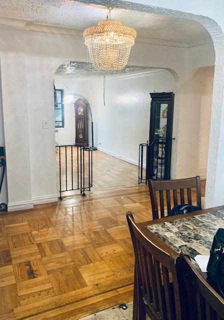 dining space featuring baseboards, arched walkways, a chandelier, and a textured ceiling