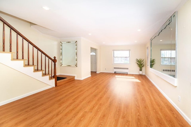 unfurnished living room featuring baseboards, stairway, light wood-type flooring, and radiator