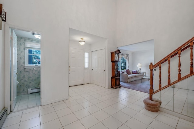 foyer with a baseboard heating unit, a high ceiling, stairway, and light tile patterned flooring