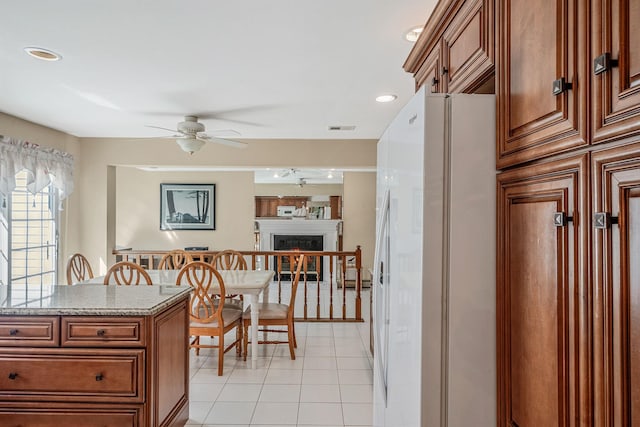 kitchen featuring light tile patterned floors, visible vents, freestanding refrigerator, ceiling fan, and a warm lit fireplace