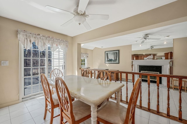 dining area featuring light tile patterned floors, a fireplace, baseboards, and a ceiling fan