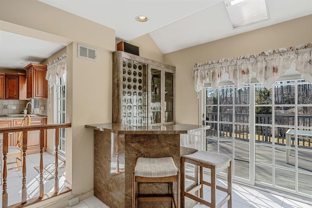 interior space featuring light tile patterned floors, visible vents, vaulted ceiling, backsplash, and recessed lighting