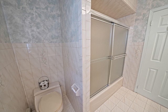 full bathroom featuring toilet, a shower with door, tile walls, and tile patterned floors