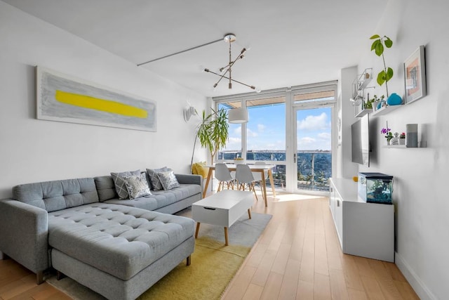 living area featuring an inviting chandelier, baseboards, a wall of windows, and wood finished floors