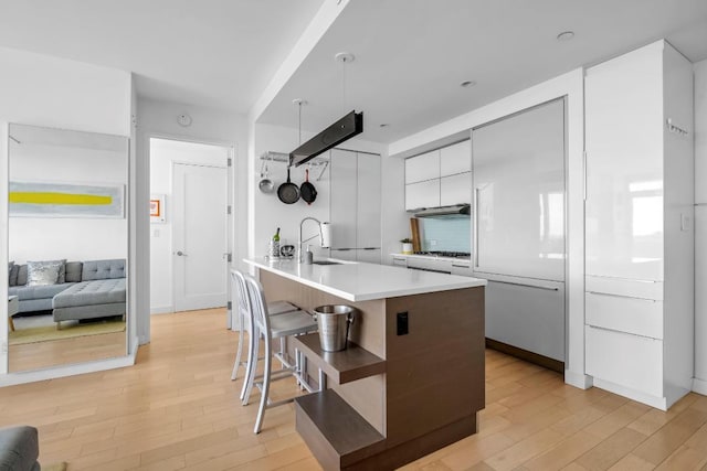 kitchen featuring light wood finished floors, white cabinets, modern cabinets, a breakfast bar area, and a sink