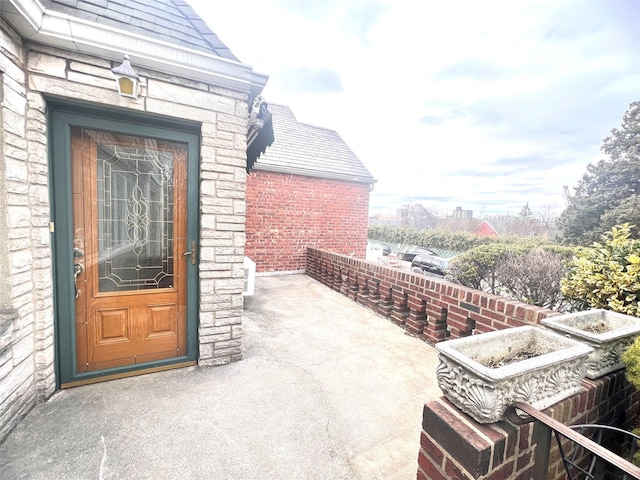 property entrance featuring stone siding, brick siding, and roof with shingles