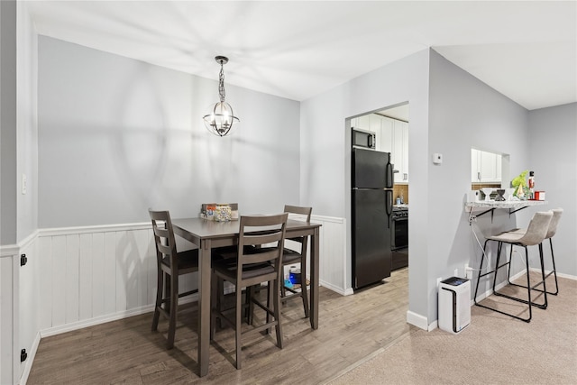 dining area with wainscoting, light wood finished floors, and an inviting chandelier