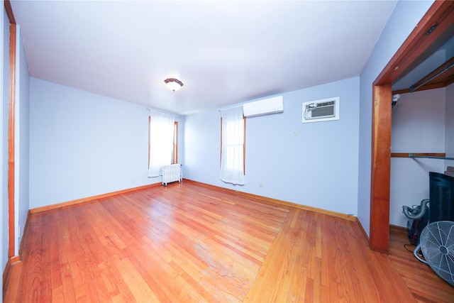 unfurnished bedroom featuring a wall unit AC, radiator, baseboards, light wood-style flooring, and a wall mounted air conditioner