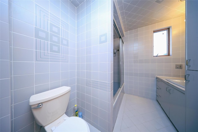 full bath featuring vanity, tile walls, toilet, and bath / shower combo with glass door