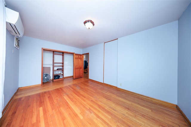 unfurnished bedroom featuring a wall unit AC, light wood-style flooring, and baseboards