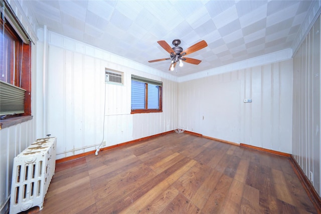 empty room featuring baseboards, radiator heating unit, a wall unit AC, hardwood / wood-style flooring, and a ceiling fan