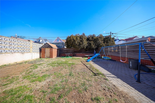 view of yard with an outbuilding, a patio, a fenced backyard, a storage shed, and a playground