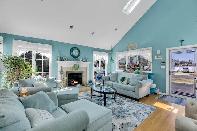 living area featuring high vaulted ceiling, a tile fireplace, a skylight, and wood finished floors