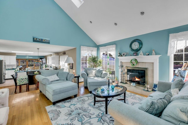 living room with high vaulted ceiling, a tile fireplace, and light wood-style flooring