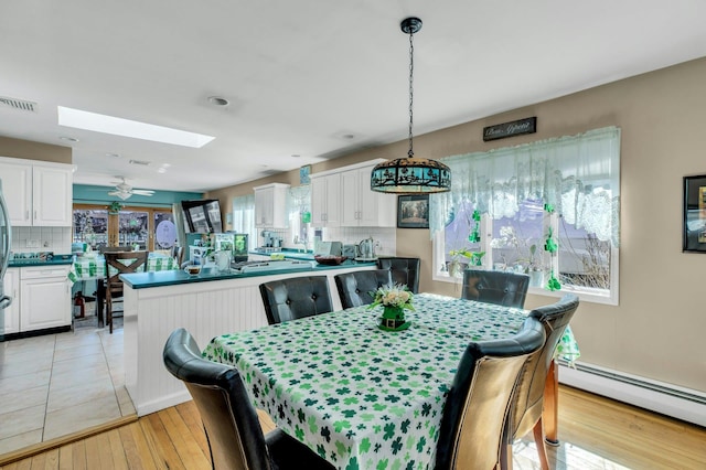 dining room featuring a baseboard heating unit, light wood finished floors, a skylight, and visible vents