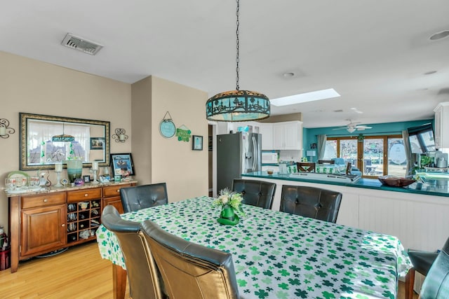 dining room featuring light wood finished floors, ceiling fan, a skylight, and visible vents