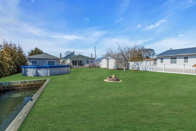 view of yard with a fenced in pool, a storage shed, an outdoor fire pit, a fenced backyard, and an outdoor structure