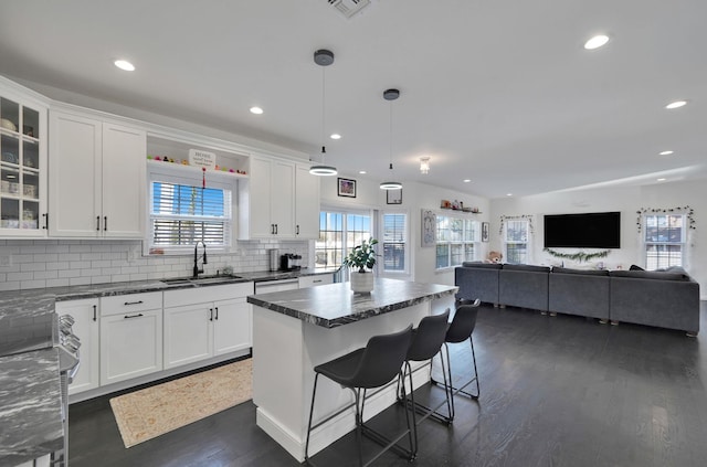 kitchen with a sink, white cabinets, glass insert cabinets, tasteful backsplash, and a center island