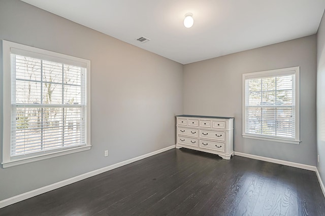 empty room with visible vents, dark wood-type flooring, and baseboards