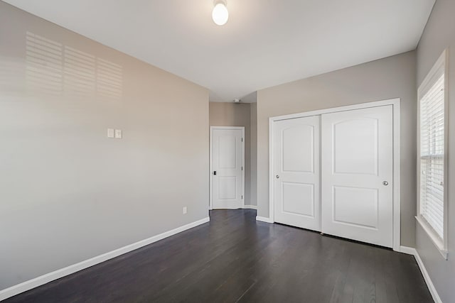 unfurnished bedroom with a closet, baseboards, and dark wood-style floors