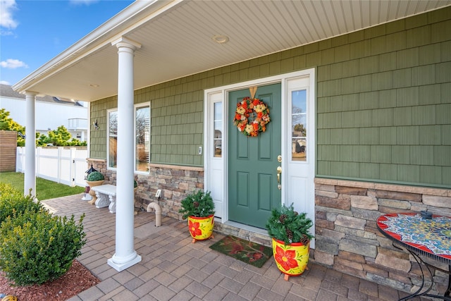 entrance to property with covered porch, fence, and stone siding