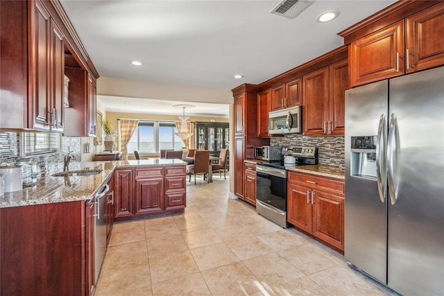 kitchen featuring visible vents, light stone countertops, appliances with stainless steel finishes, a peninsula, and a sink