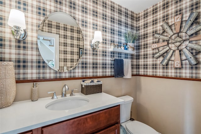 bathroom featuring vanity, toilet, and wallpapered walls