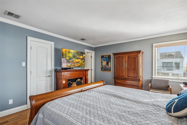 bedroom with wood finished floors, crown molding, a fireplace, and visible vents