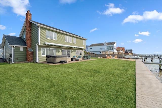 rear view of house with a yard, a patio, a chimney, and a hot tub