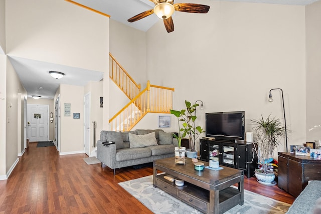 living room featuring wood finished floors, a high ceiling, baseboards, and stairs