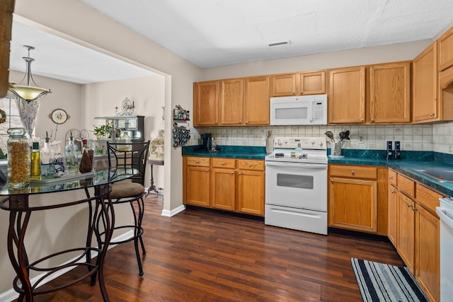 kitchen with dark wood-type flooring, dark countertops, white appliances, and visible vents