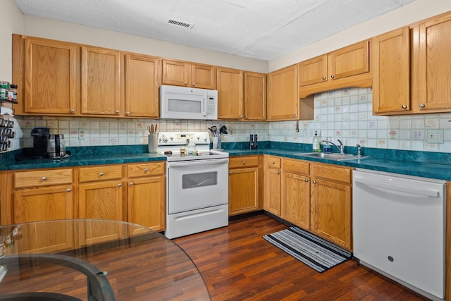 kitchen featuring dark countertops, white appliances, dark wood-style floors, and a sink