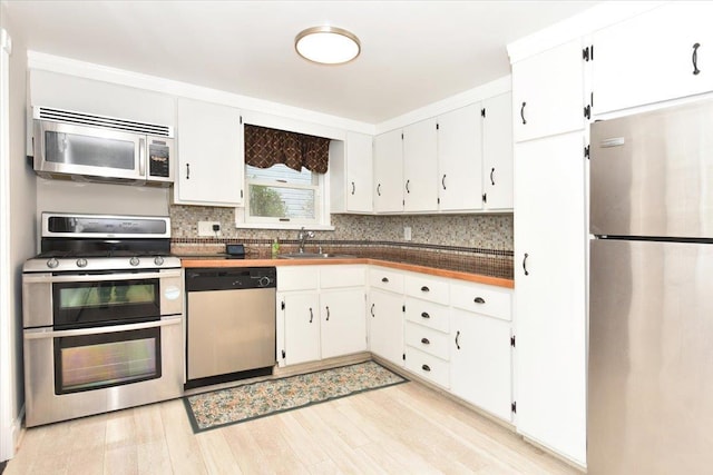 kitchen with a sink, white cabinetry, appliances with stainless steel finishes, light wood finished floors, and tasteful backsplash