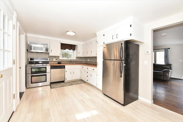 kitchen with white cabinets, backsplash, stainless steel appliances, light wood-type flooring, and a sink