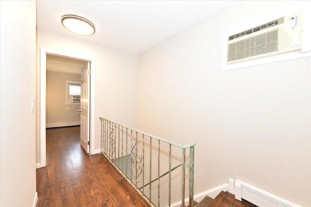 hall featuring a baseboard heating unit, wood finished floors, an upstairs landing, baseboards, and a wall mounted AC