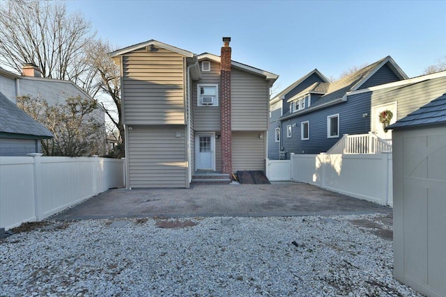 rear view of house with entry steps, a chimney, fence, and a patio