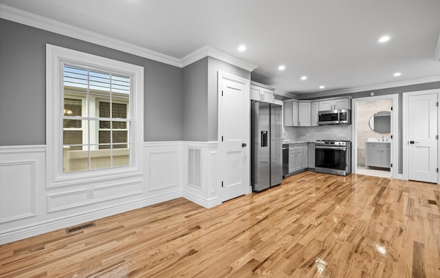 kitchen with ornamental molding, appliances with stainless steel finishes, backsplash, and light wood-style flooring