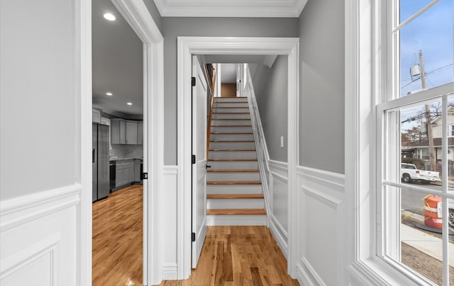 stairway with a wainscoted wall, ornamental molding, wood finished floors, and a decorative wall