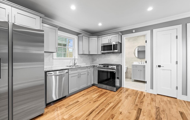 kitchen featuring appliances with stainless steel finishes, crown molding, a sink, and gray cabinetry