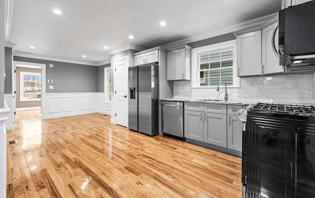 kitchen with light stone counters, light wood finished floors, stainless steel appliances, gray cabinets, and a sink