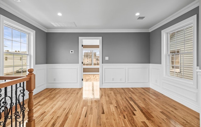 spare room featuring a wainscoted wall, light wood-style flooring, visible vents, and ornamental molding