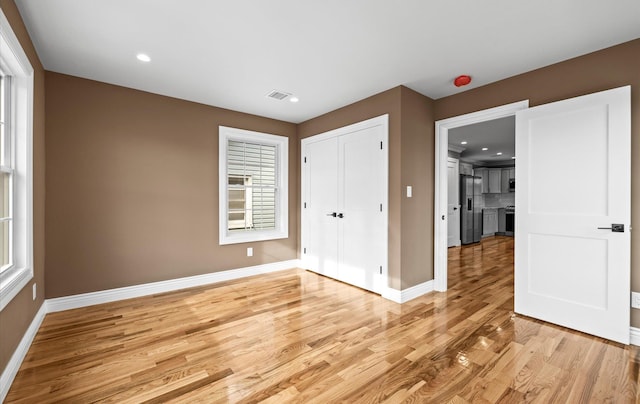 unfurnished bedroom featuring light wood finished floors, a closet, stainless steel fridge, and baseboards