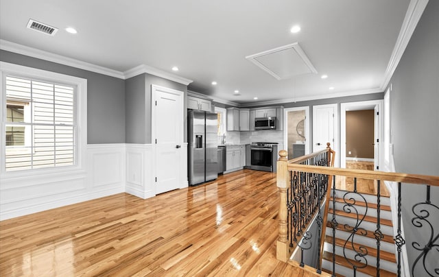 kitchen with gray cabinetry, visible vents, appliances with stainless steel finishes, wainscoting, and light wood finished floors