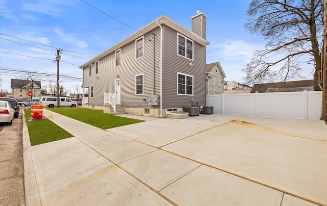 back of property with entry steps, central AC, a chimney, and fence