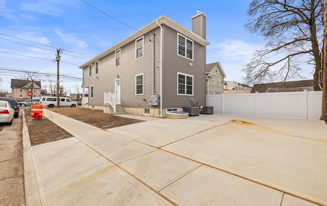 view of side of home featuring entry steps, a chimney, fence, and cooling unit