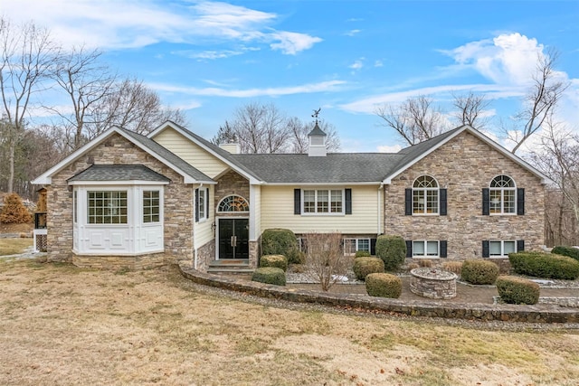 view of front of house featuring a front lawn, an outdoor fire pit, roof with shingles, and a chimney