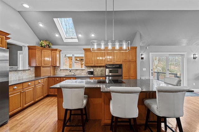 kitchen featuring a center island, light wood-type flooring, vaulted ceiling with skylight, appliances with stainless steel finishes, and a sink