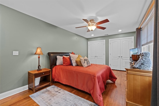 bedroom with wood finished floors, baseboards, two closets, and ceiling fan